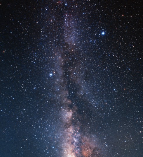 Pohled do středu naší Galaxie na širokoúhlém záběru letní Mléčné dráhy. V horní části je patrný obrazec Letního trojúhelníku, ve spodní části souhvězdí Střelce. Červené skvrnky představují mlhoviny zářícího vodíku, patrný je i komplikovaný systém neprůhledných oblaků mezihvězdné látky. Samozřejmě, že takto barevně a podrobně Mléčnou dráhu na vlastní oči nezahlédnete. Zdroj: Akira Fujii.